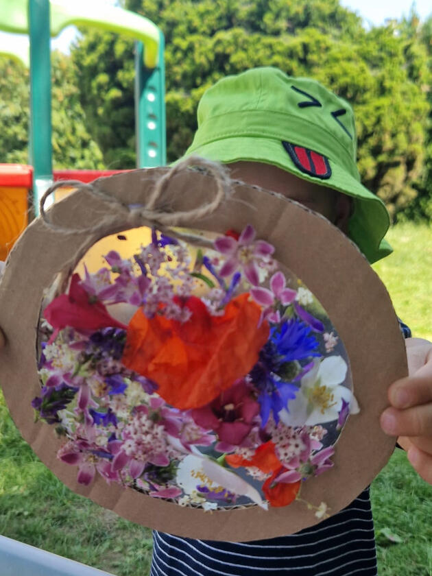 Dziecko prezentujące pracę plastyczną z kwiatów w ogrodzie Żłobka Mariposa
